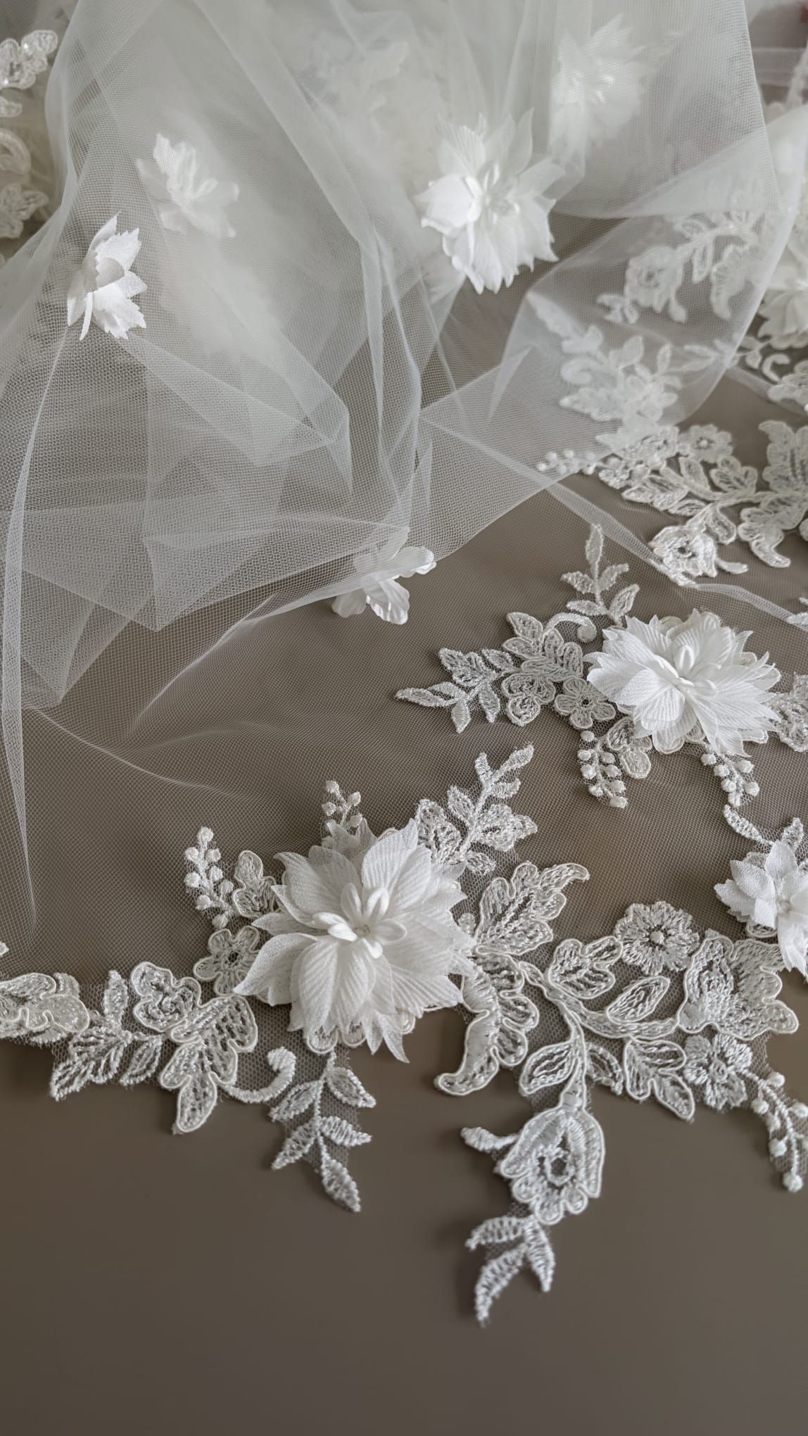 Detalle de apliques de encaje floral en 3D con blonda ondulada sobre tul diamante blanco natural de alta costura.