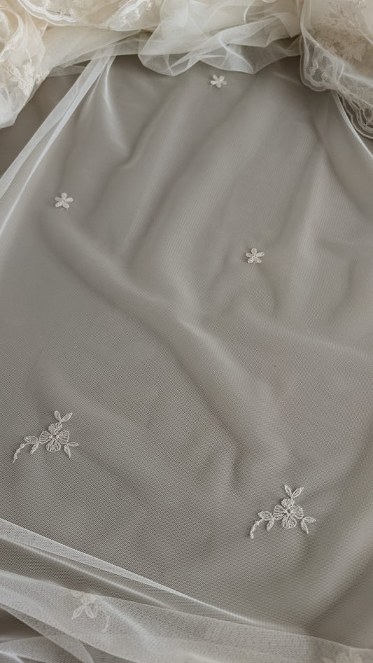Detalle de pequeñas flores y ramitas bordadas en relieve en color marfil sobre el cuerpo de tul de una mantilla nupcial.