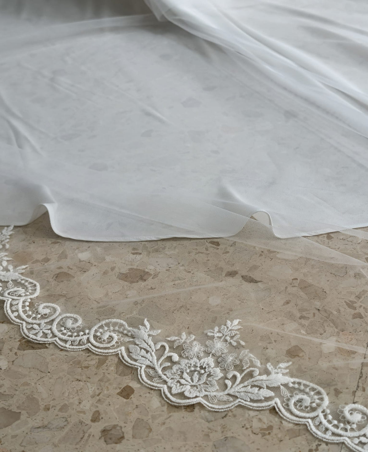 Detalle en primer plano del encaje de algodón con motivos florales y ondas sobre tul soft blanco natural en el velo de novia amantillado 9156.