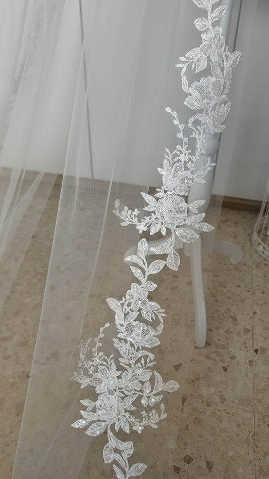 Detalle vertical de una blonda continua con motivos de hojas y flores que sube por el lateral de un velo de novia.