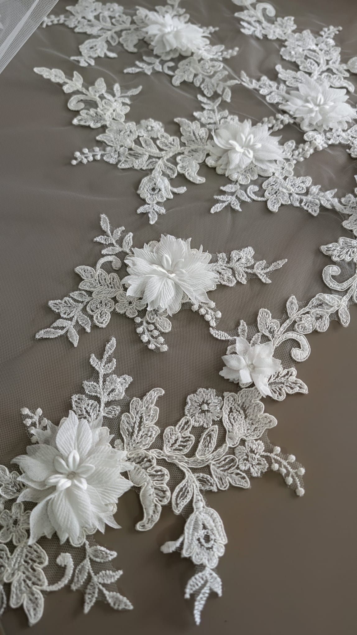 Primer plano de flores tridimensionales de tela y bordados de hojas en relieve sobre el contorno de un velo de novia de Zulema Torres.