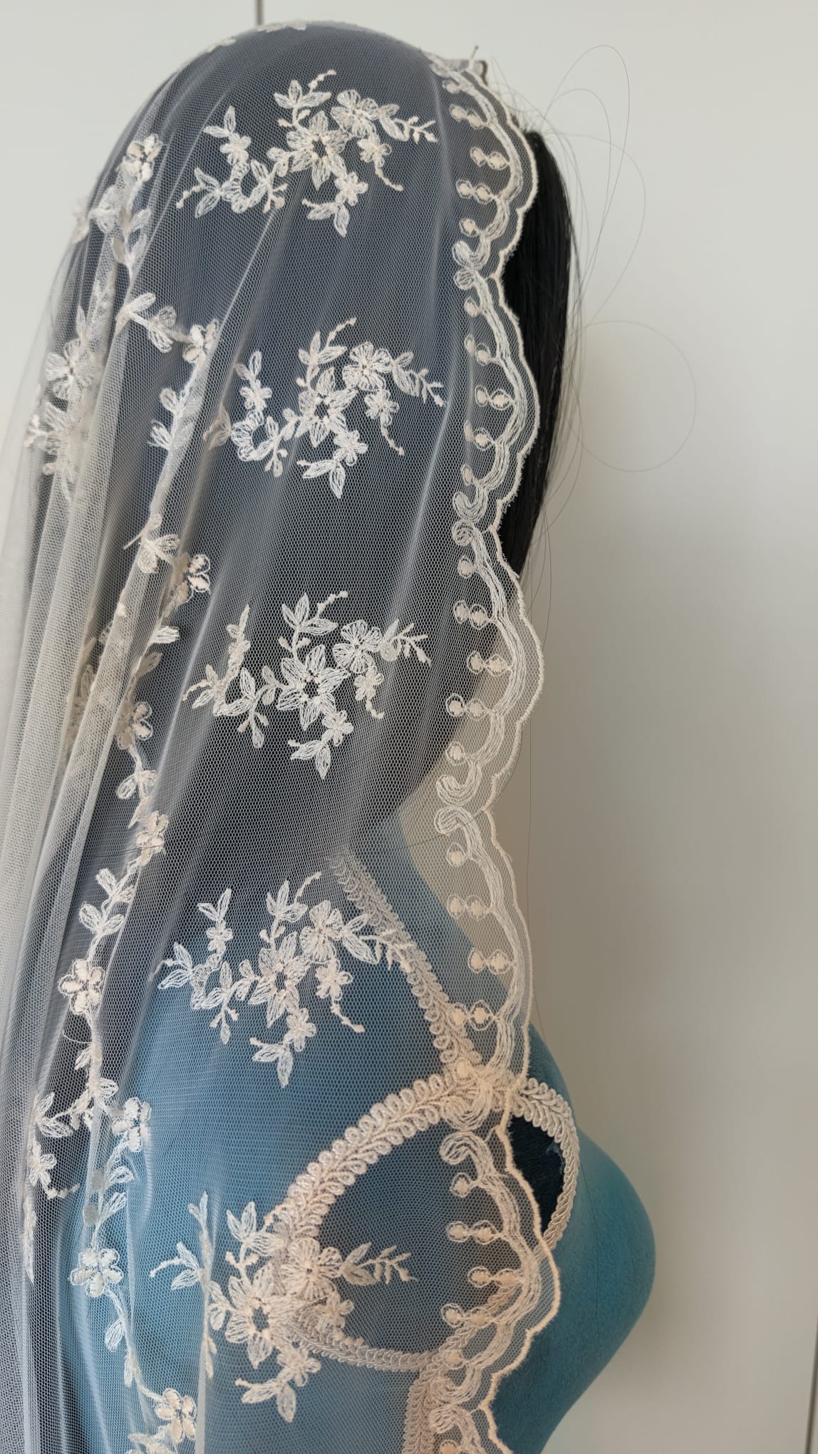Plano lateral de la mantilla de novia Ronda con borde festoneado de ondas cubriendo la cabeza de un maniquí.