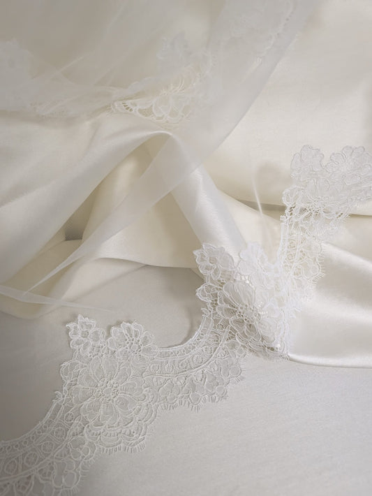 Primer plano de encaje rebrodé floral con sutiles lentejuelas brillantes sobre tul sedoso blanco natural.
