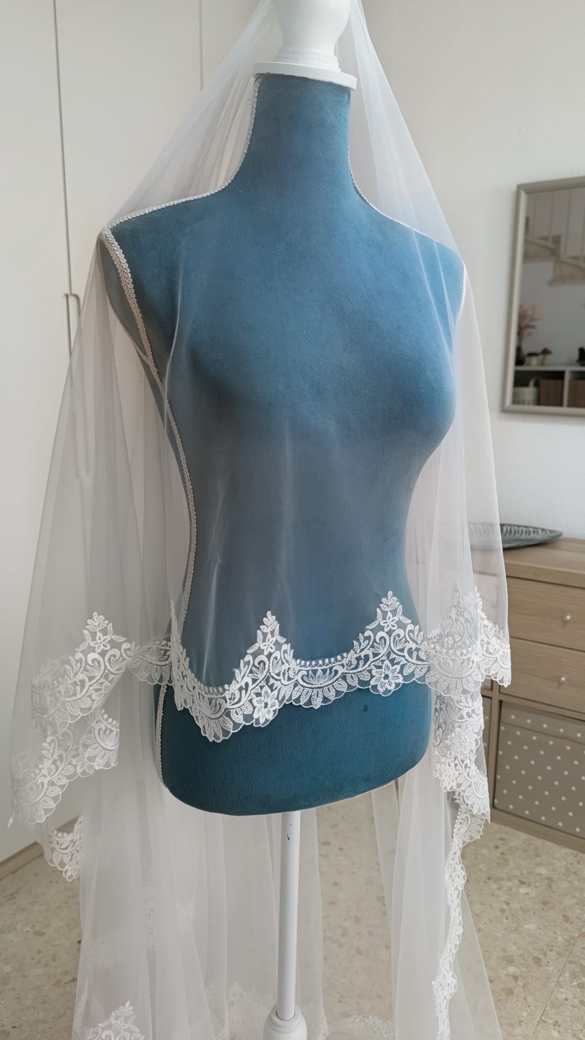 Primer plano lateral de una blonda de encaje de algodón con motivos de flores y hojas sobre tul de novia blanco natural.